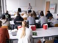 Veranstaltungsbericht Ein junger Mann steht vor einem vollen Klassenraum und hält einen Vortrag.
