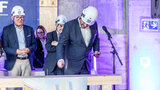 Richtfest Martin Bornträger schlägt mit einem Hammer einen Nagel in den symbolischen Dachbalken. Im Hintergrund sind drei weitere Personen zu sehen.