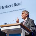 Graduierungsfeier Gelsenkirchen 2025 Herbert Reul am Rednerpult vor einer großen Leinwand, auf der sein Name steht.